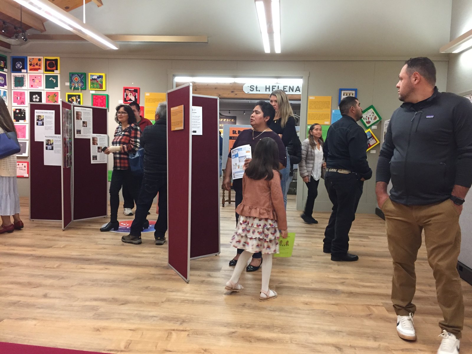 A crowd gathered among display panels and colorful artwork in the Heritage Center’s rotating exhibit room.